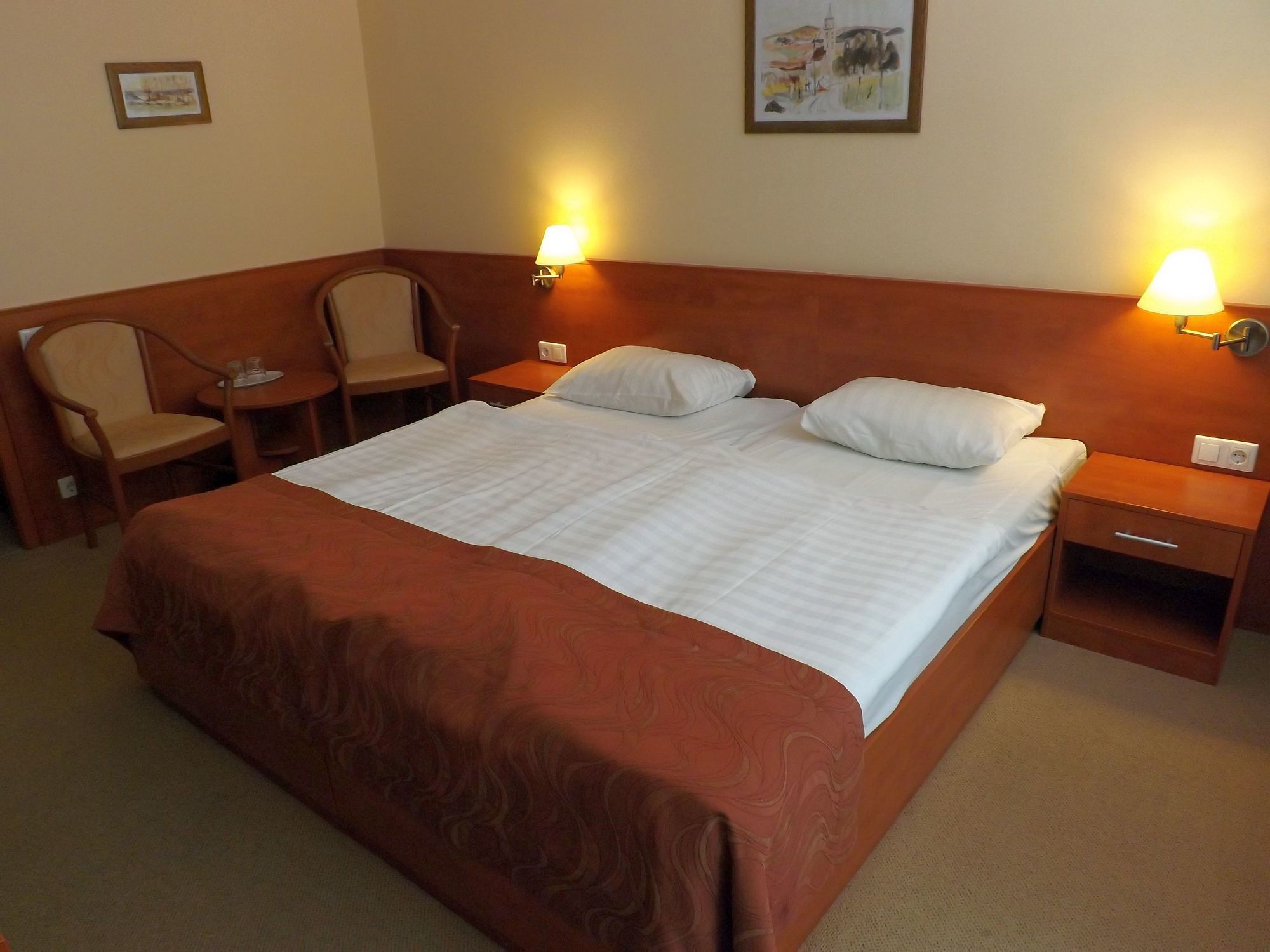 Een hotelkamer met een groot bed, twee nachtkastjes, een stoel en twee wandlampen.