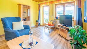 Uma sala de estar com um sofá azul, um aparador de madeira e uma janela grande com cortinas.