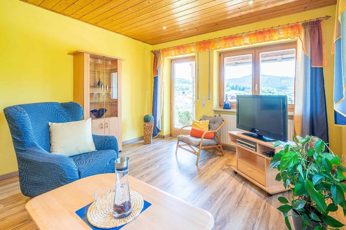 A living room with a blue sofa, a wooden TV stand, and a large window with curtains.