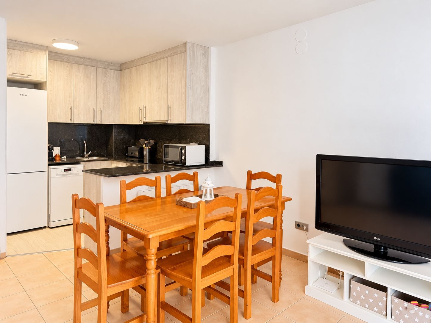 A compact kitchen with a dining table and chairs, a microwave, and a flat-screen TV on a stand.