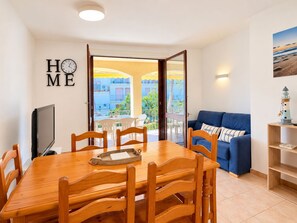 Une pièce comprenant une table à manger, des chaises, un canapé, un téléviseur et donnant sur l’extérieur.