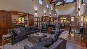 A spacious living room with a large sectional sofa, multiple chairs, and a dining area with wooden cabinets and a chandelier.