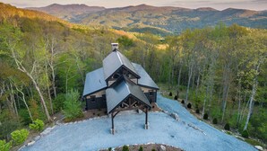 A cabin with a sloped roof, surrounded by a forested landscape.