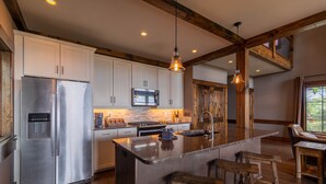 Une cuisine moderne dotée d’appareils électroménagers en acier inoxydable, de poutres en bois et d’un grand îlot central avec des tabourets.