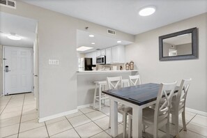 A modern kitchen with white cabinets, a dark countertop, and a dining area with white chairs and a dark table.