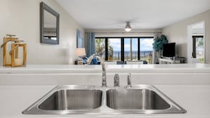A modern kitchen with a double sink, a ceiling fan, and a view of the beach through large windows. - Beachfront, ground-level condo in a gated resort with a pool, beach access, and Free Activities! (Panama City Beach)