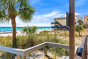 A beach view with a wooden deck, palm trees, and a building with a balcony overlooking the ocean. - Beachfront, ground-level condo in a gated resort with a pool, beach access, and Free Activities! (Panama City Beach)