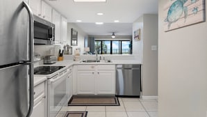 A modern kitchen with white cabinets, stainless steel appliances, and a large window offering a view of the outdoors. - Beachfront, ground-level condo in a gated resort with a pool, beach access, and Free Activities! (Panama City Beach)