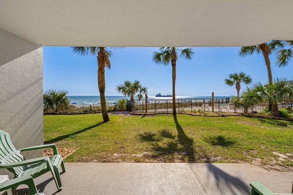 A covered patio with a view of the beach, palm trees, and a ship in the distance. - Beachfront, ground-level condo in a gated resort with a pool, beach access, and Free Activities! (Panama City Beach)