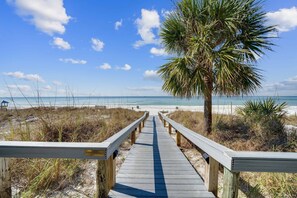 A wooden boardwalk leading to a beach with a palm tree and sandy dunes. - Beachfront, ground-level condo in a gated resort with a pool, beach access, and Free Activities! (Panama City Beach)