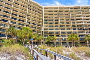A multi-story hotel with balconies, a sandy beach area, and a wooden walkway. - Beachfront, ground-level condo in a gated resort with a pool, beach access, and Free Activities! (Panama City Beach)
