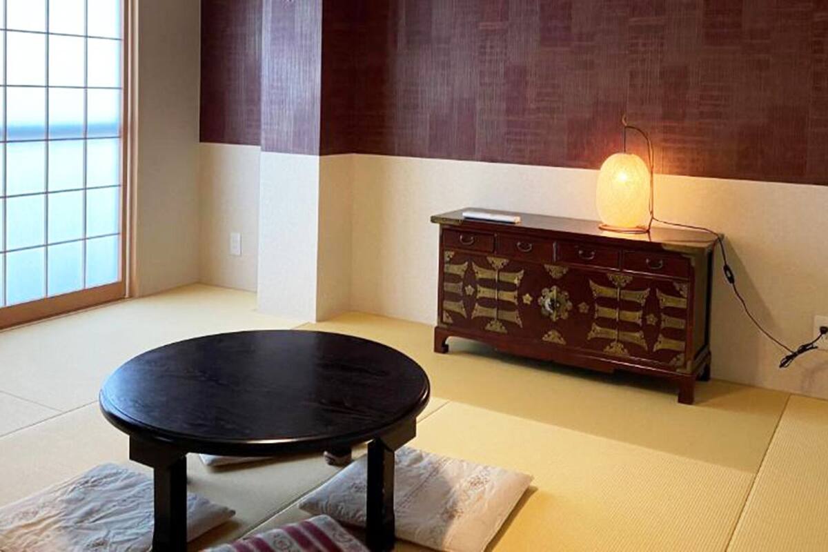 Una habitación con tatami, una mesa de madera baja, un aparador tradicional y un puertas correderas de vidrio.
