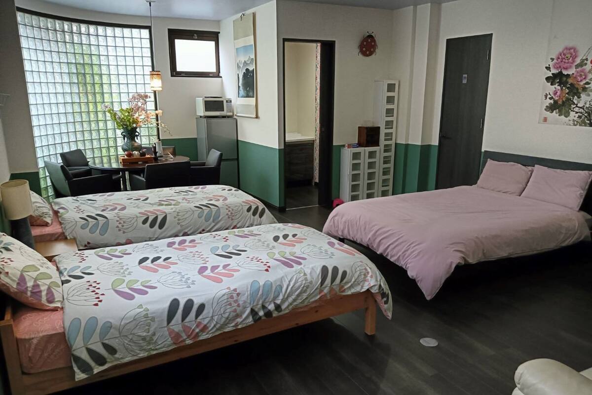 Un dormitorio con dos camas, un escritorio, una silla, un microondas y una mesita con un florero.