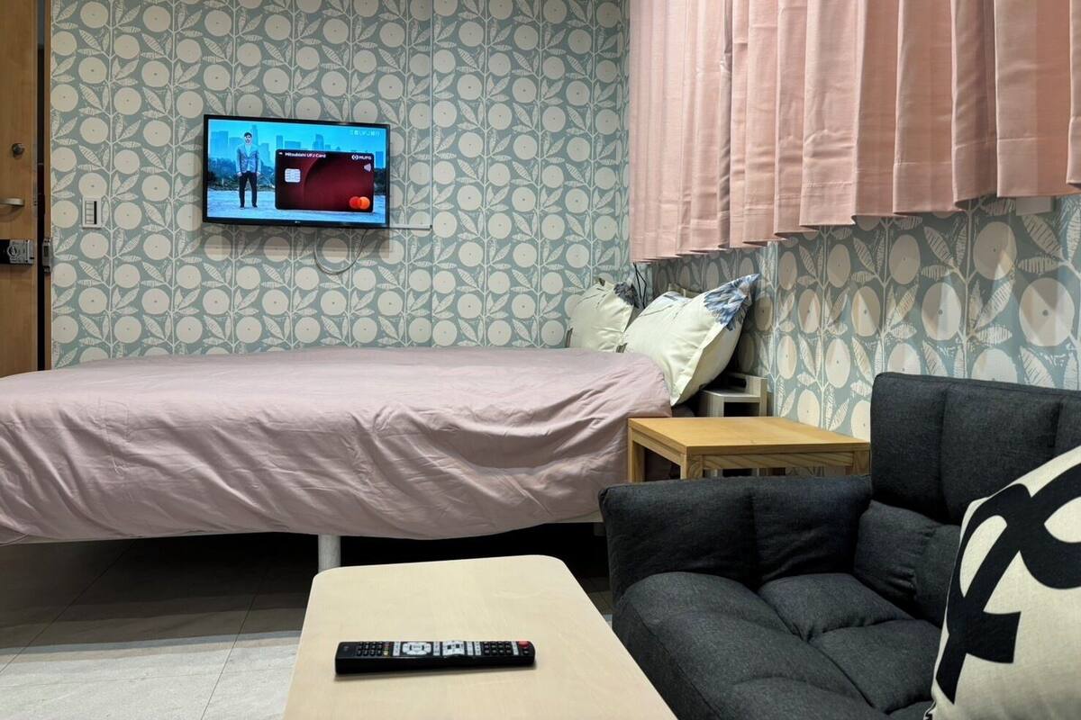 Una habitación con cama, sofá, televisor montado en la pared y control remoto sobre una mesa.