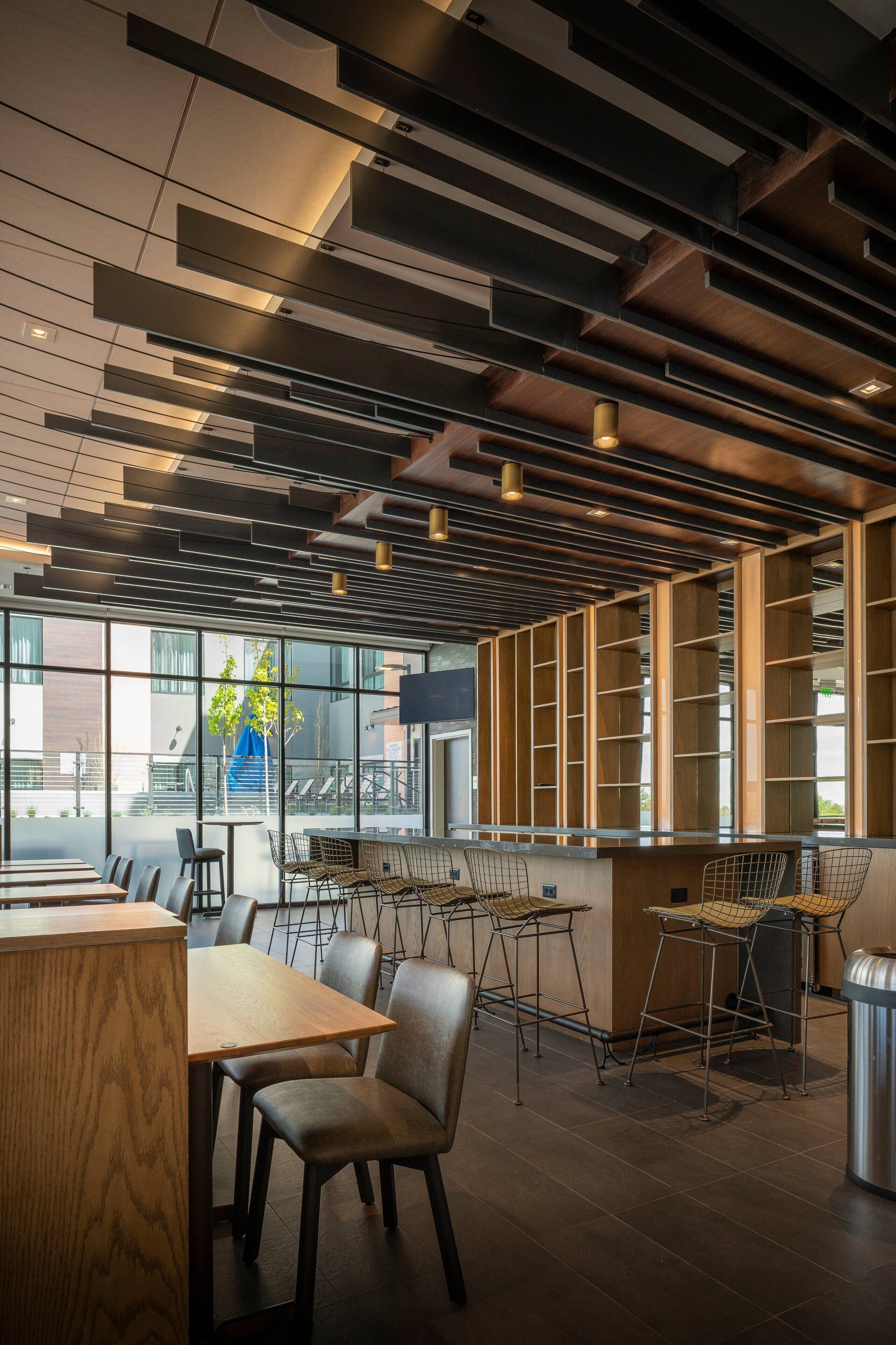 Ein modernes Interieur mit Holztischen und -stühlen, einer Bar und großen Fenstern mit Blick ins Freie.