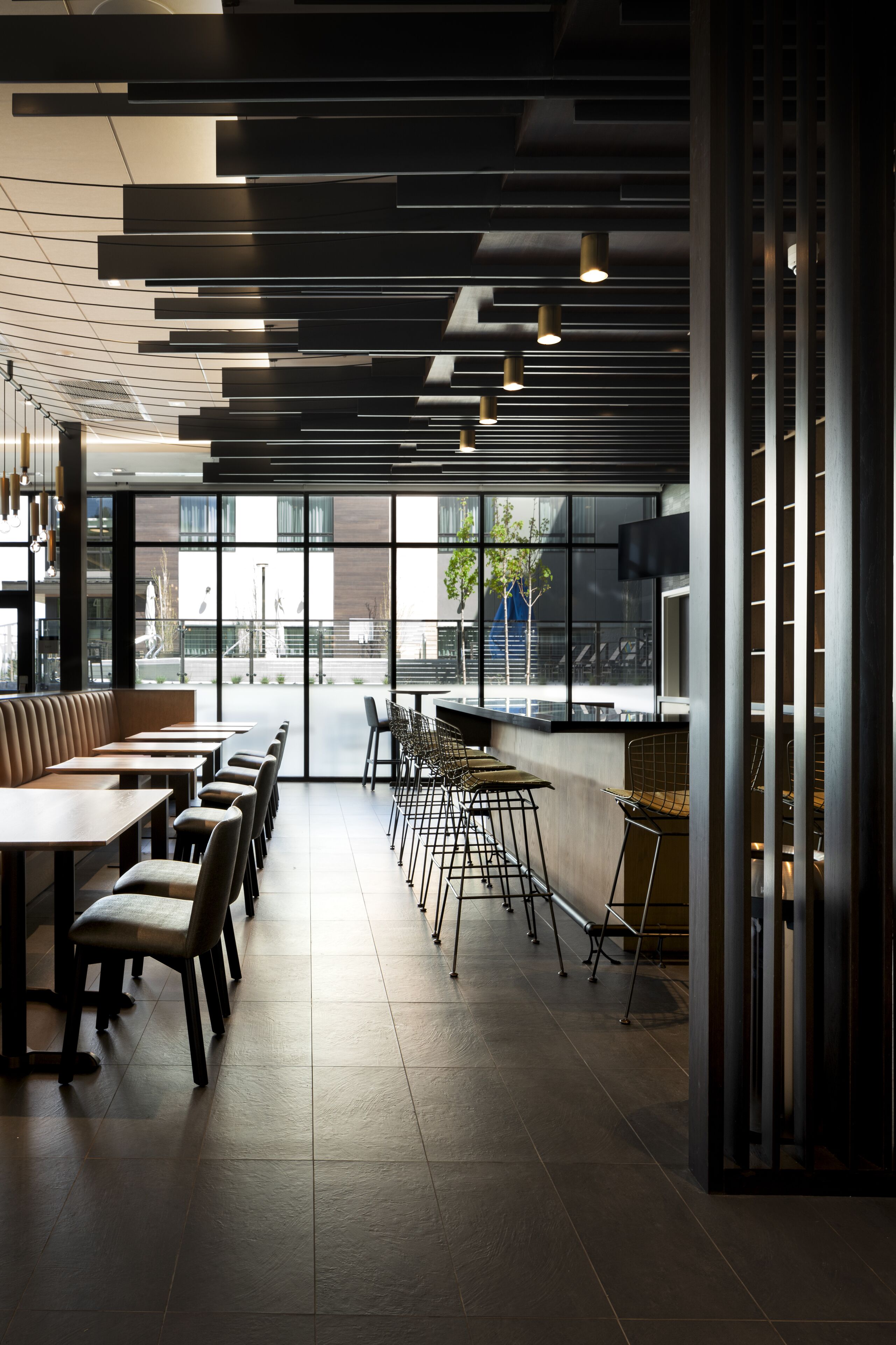 Een modern restaurantinterieur met hoge plafonds, zichtbare leidingen en een combinatie van zitbanken en barplaatsen.