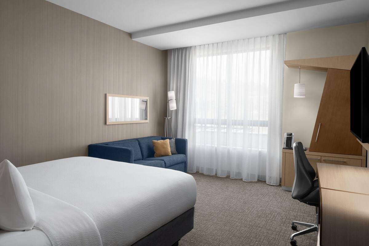 A hotel room with a large bed, a blue sofa, a desk, and a TV.