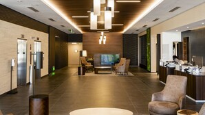 A lobby with a modern design, featuring a central seating area with a round coffee table and armchairs, a television, and a reception desk. - Courtyard by Marriott Salt Lake City Cottonwood (Salt Lake City)