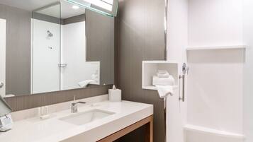 A modern bathroom with a large mirror, two sinks, a shower, and a towel rack.