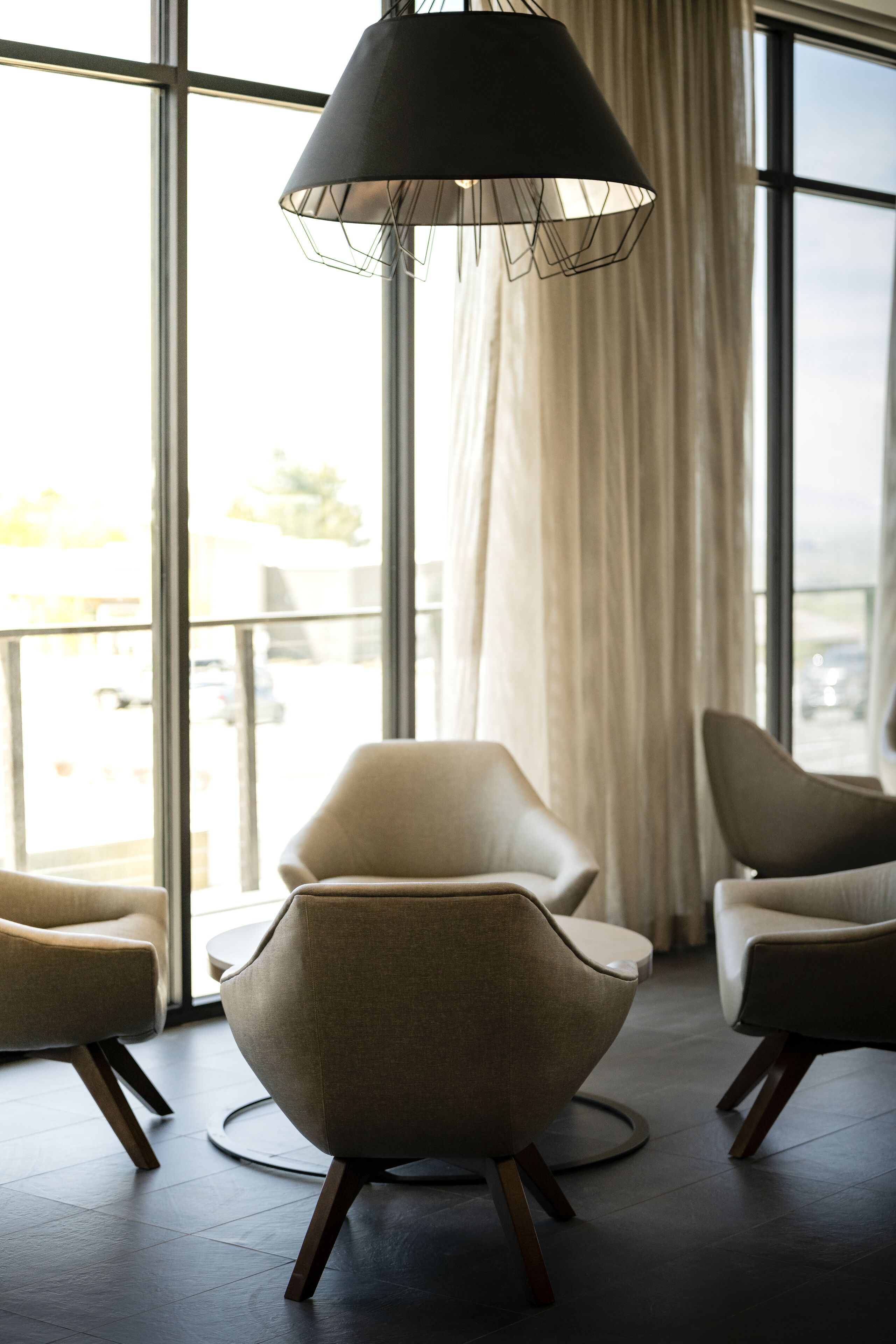 Una habitación moderna con ventanas amplias, dos sillas contemporáneas y una lámpara colgante.