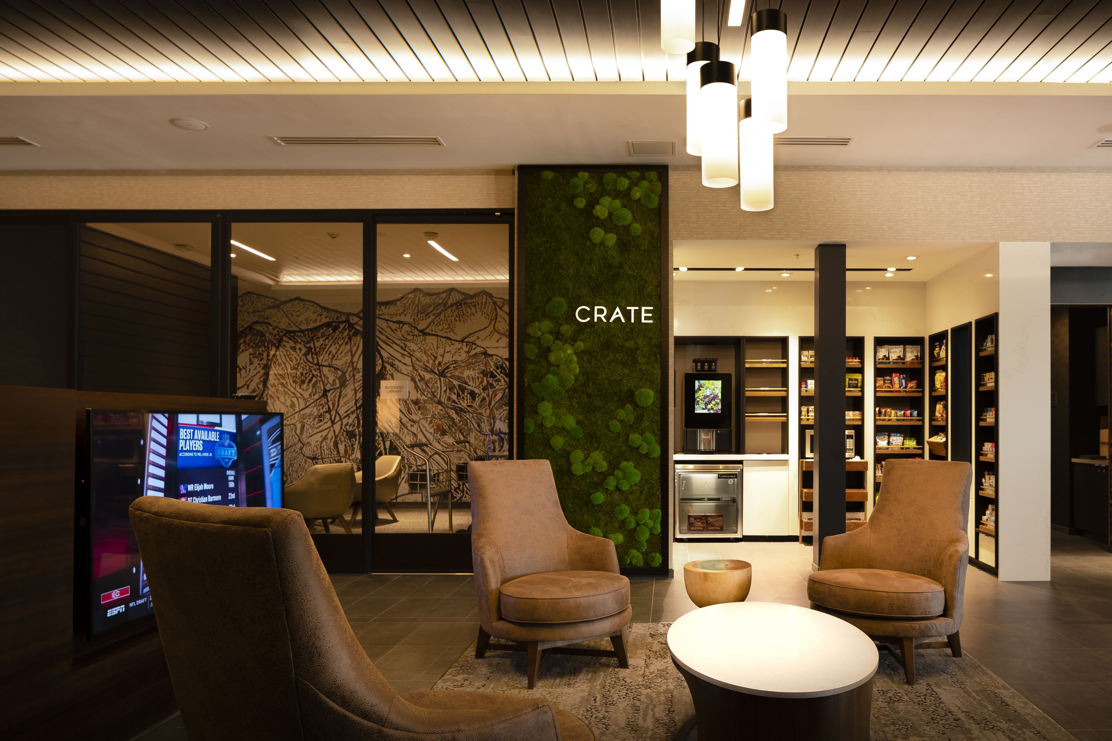Un lobby moderno con una gran pantalla digital, asientos cómodos, una pared verde con el rótulo 'CRATE' y un interior bien iluminado.