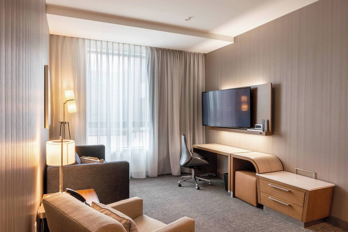 A hotel room with a bed, a desk, a chair, a TV, and a lamp.