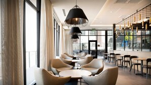 A modern interior with round tables and chairs, large windows, and hanging pendant lights. - Courtyard by Marriott Salt Lake City Cottonwood (Salt Lake City)