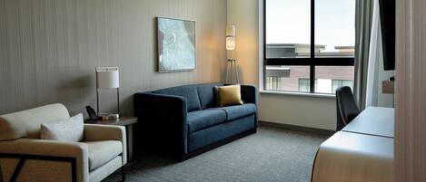 Una habitación de hotel moderna con sofá, sillón y escritorio con televisor de pantalla plana.