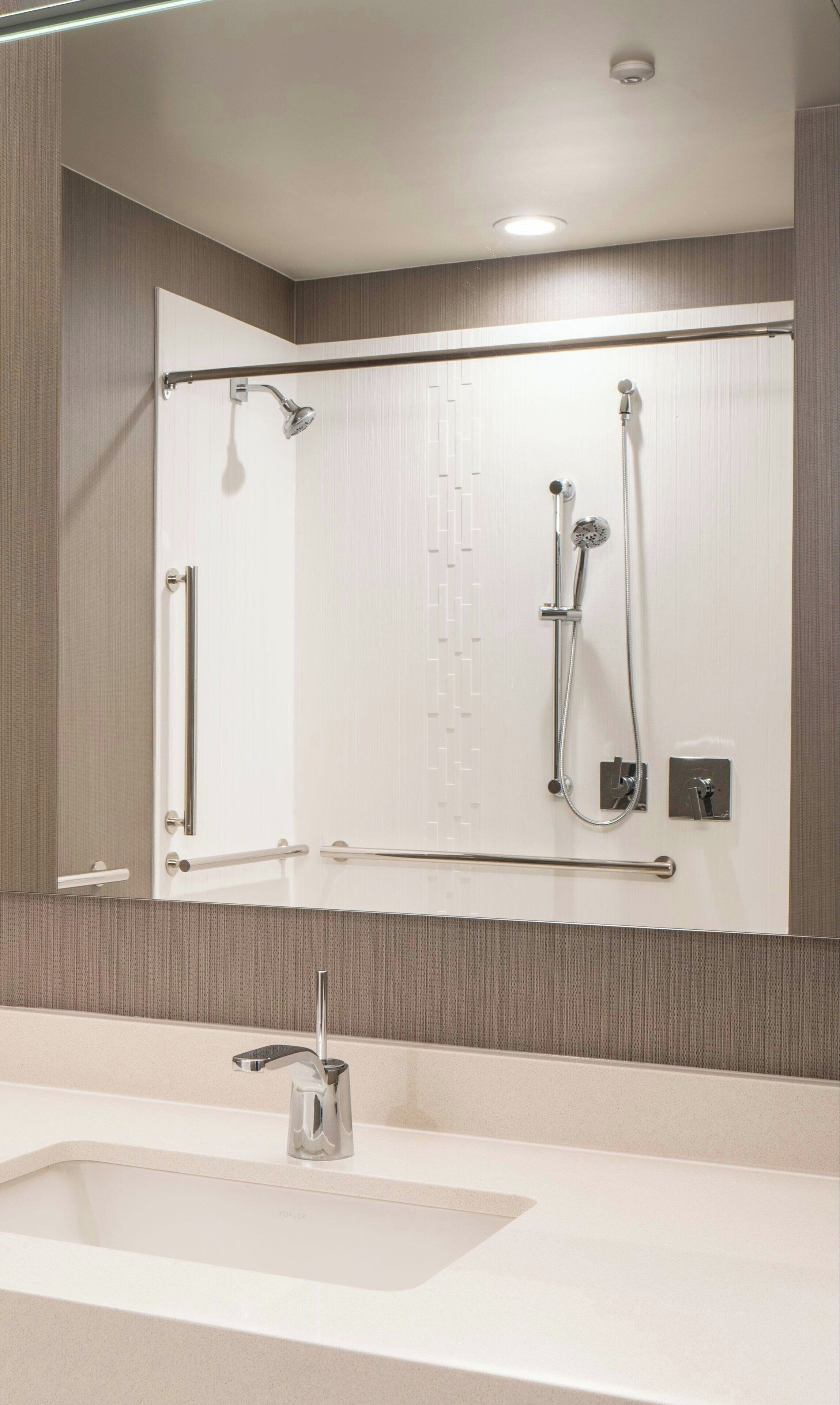 Een moderne badkamer met een grote spiegel, een douche met een handdouche, en een muurbevestigde kraan.
