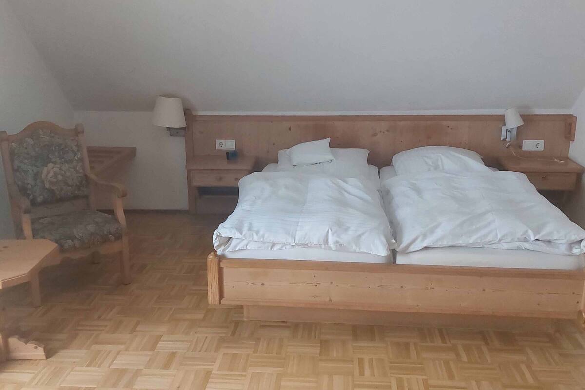 A bedroom with a wooden bed, a nightstand with a lamp, a chair, and a small table.