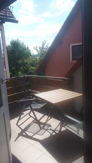 An outdoor patio with a table and chairs, a red building in the background, and trees.