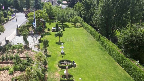 A well-maintained garden with a lawn, a fountain, and a variety of plants. - Hotel Pension Am Engelsberg (Sommerach)
