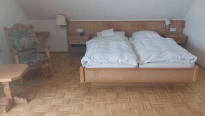 A bedroom with a wooden bed, two bedside tables with lamps, a wooden chair, and a small wooden table. - Hotel Pension Am Engelsberg (Sommerach)