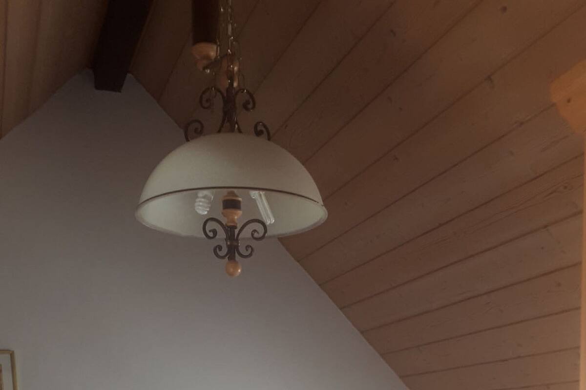 A bedroom with a wooden ceiling, a bed with white bedding, a nightstand with a lamp, and a wall-mounted light fixture.