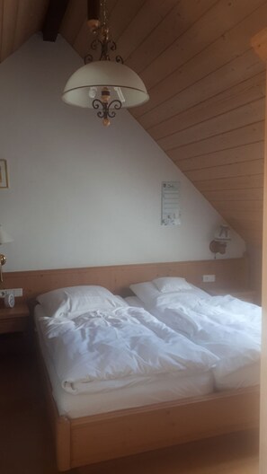 A bedroom with a wooden ceiling, a bed with white bedding, a nightstand with a lamp, and a wall-mounted light fixture.