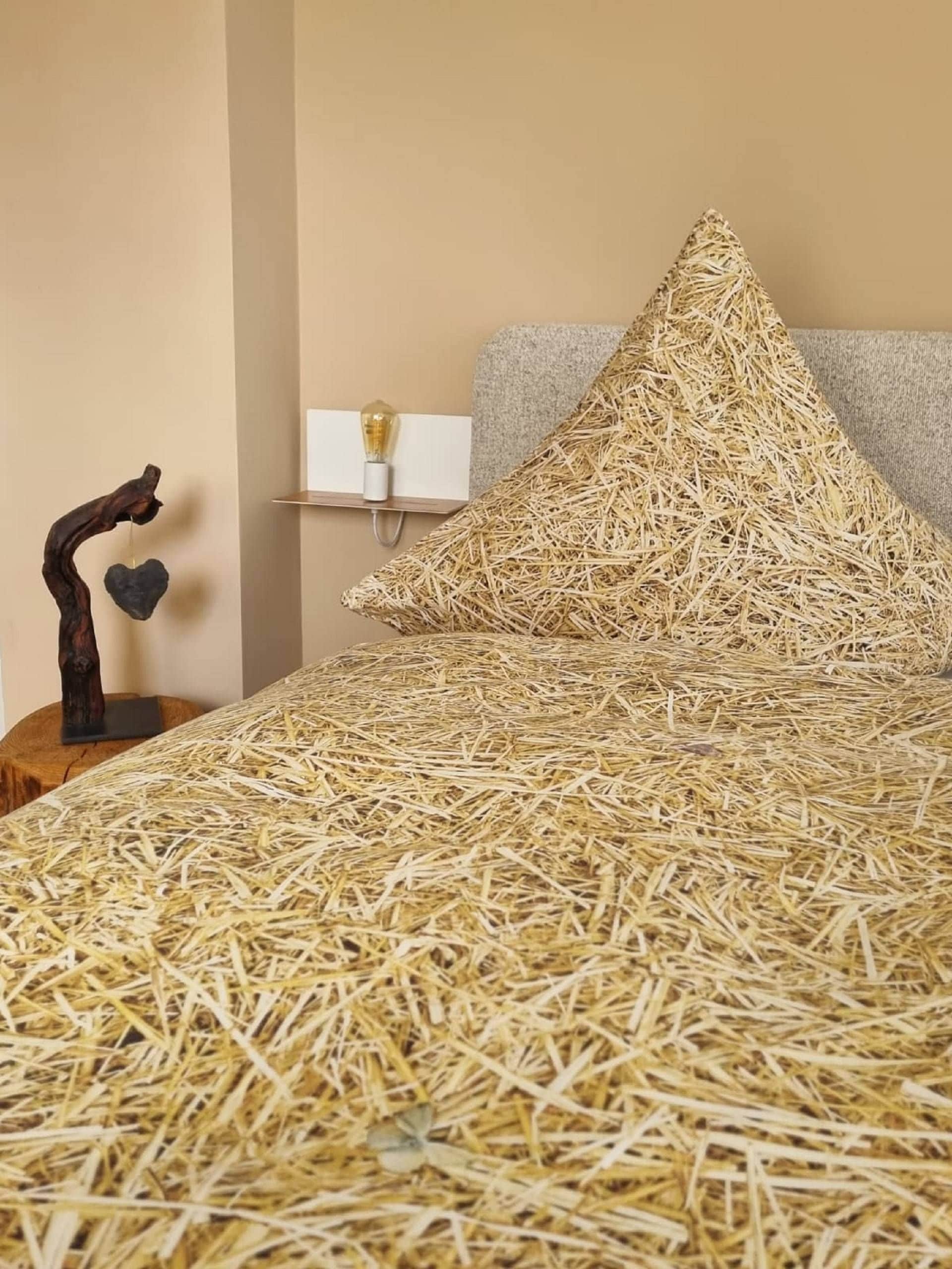 Una cama con ropa de cama similar al heno, una escultura de madera y una lámpara de pared.