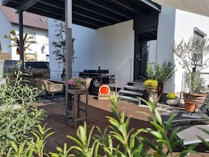 Un área de patio al aire libre con una parrilla, asientos y plantas en macetas.
