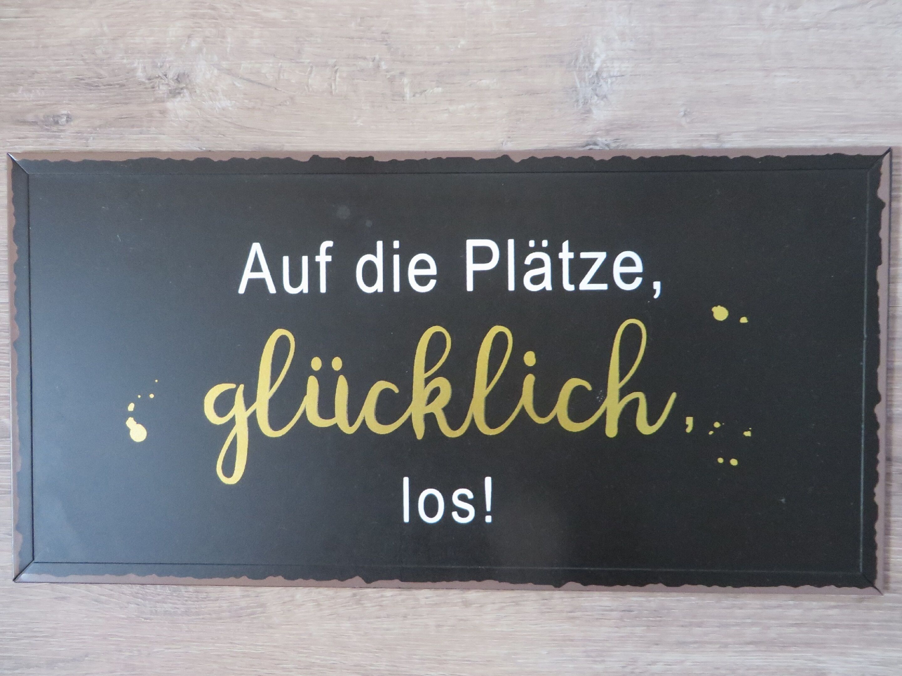 Une plaque noire avec du texte blanc et doré sur un fond en bois.