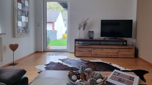 A living room with a wooden floor, a cowhide rug, a bowl of decorative items, a sofa, a television on a wooden stand, and a door leading outside. - Ferienwohnung Familie Buchner (Grossheubach)