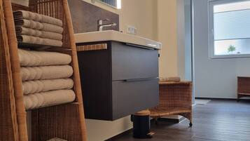 A modern bathroom with a large mirror, a dark-colored vanity, and a wicker chair with towels.