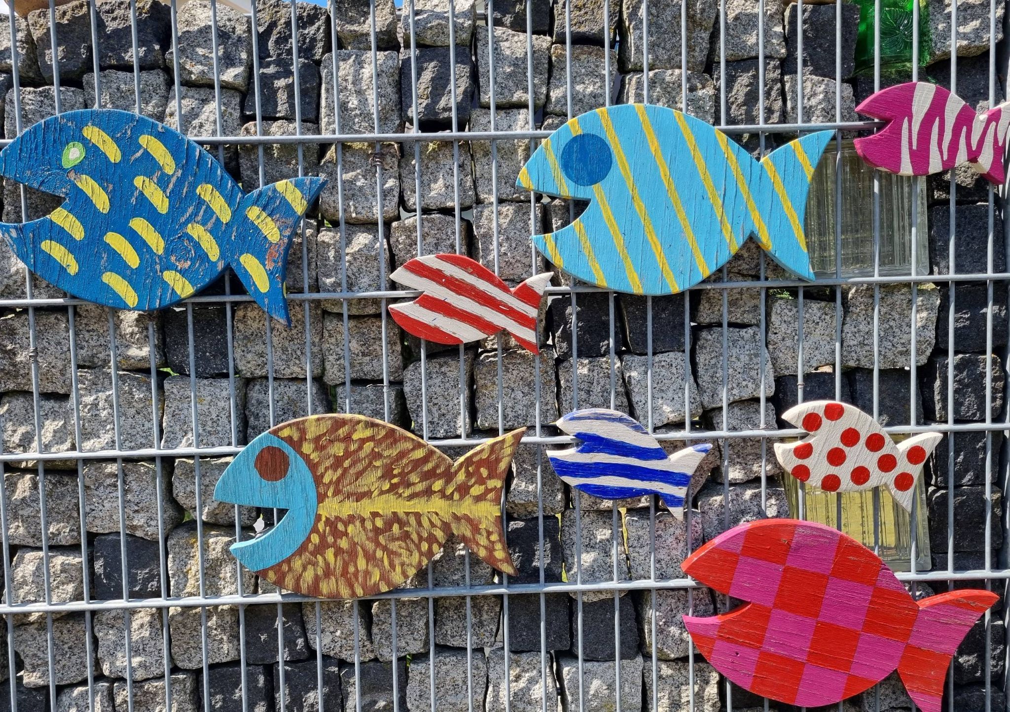 A collection of colorful fish-shaped decorations mounted on a metal fence.