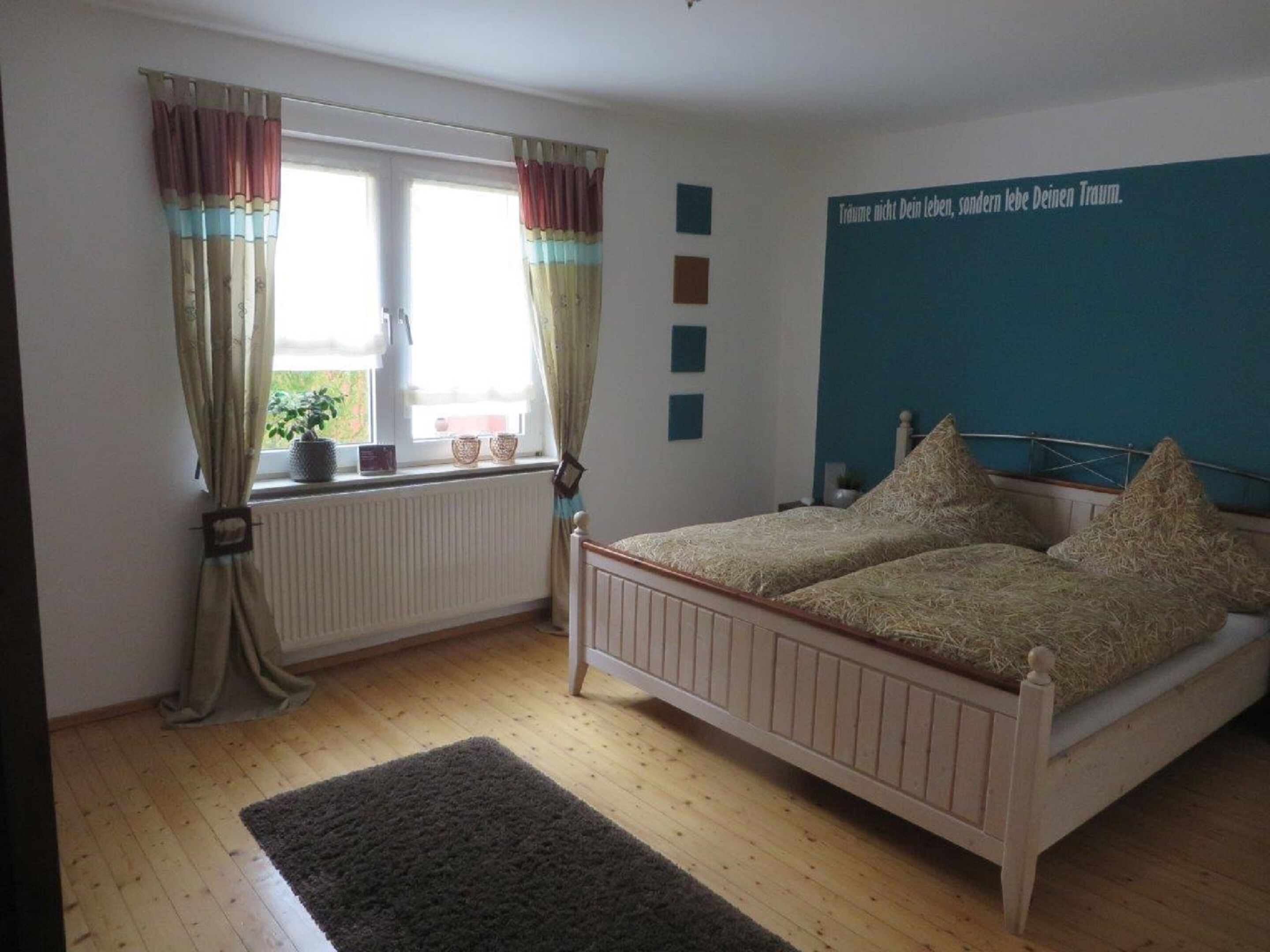 Un dormitorio con cama de madera, una ventana con cortinas, un radiador y un cartel con texto en la pared.