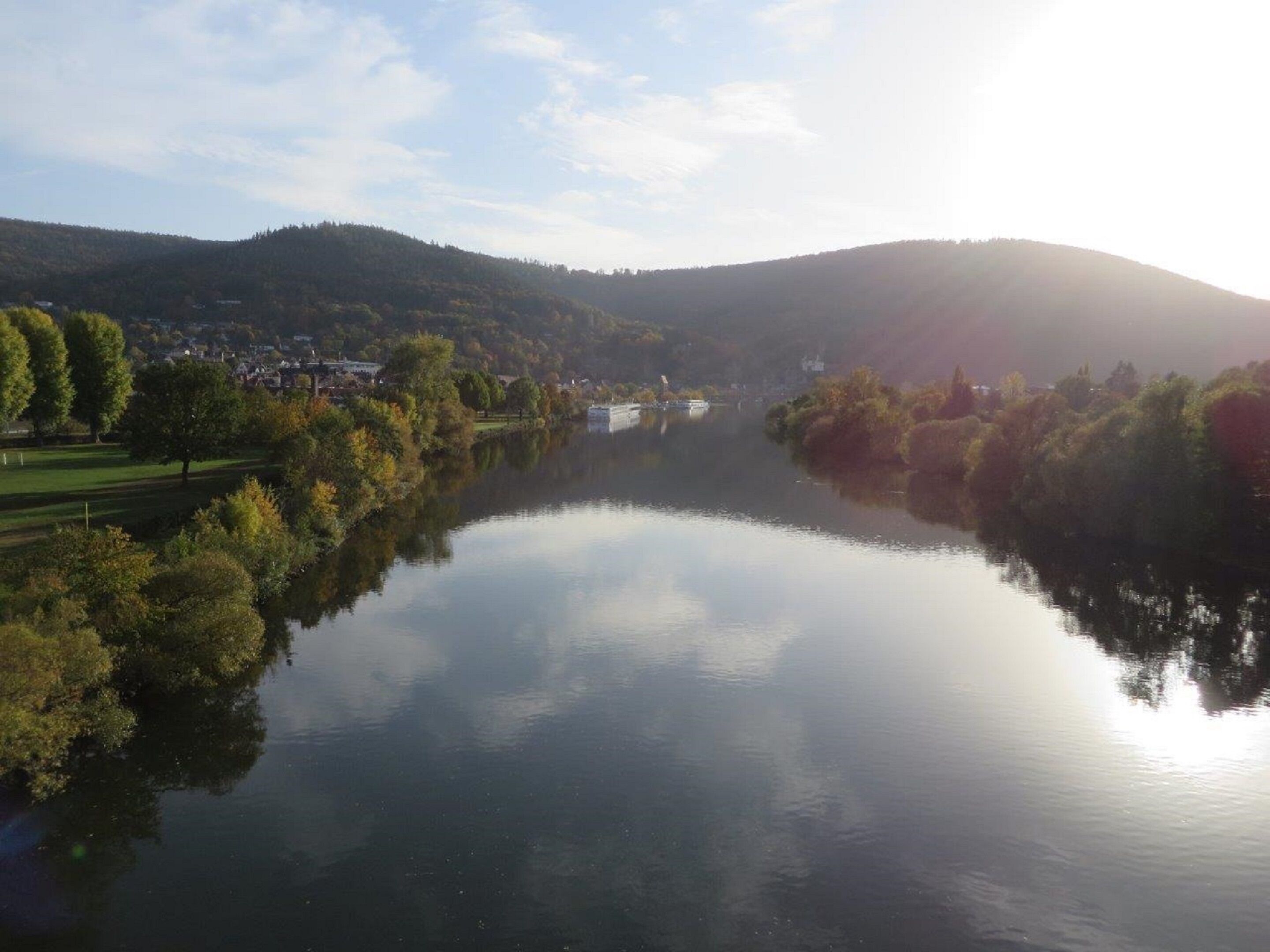 Un río tranquilo que refleja árboles y colinas, con un pueblo al fondo.