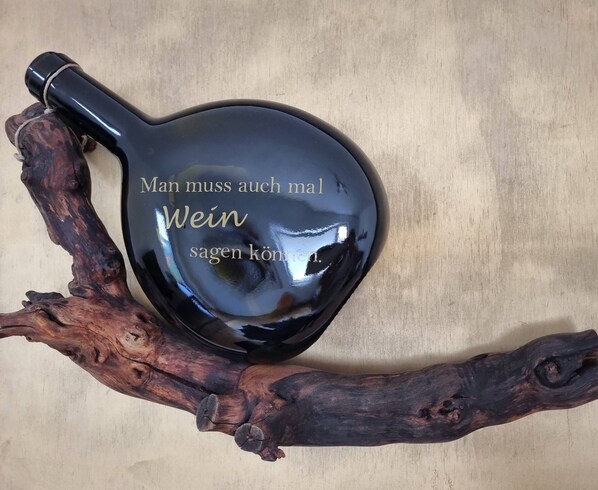 Un objeto negro y brillante con forma de corazón y texto, sobre una rama de madera.