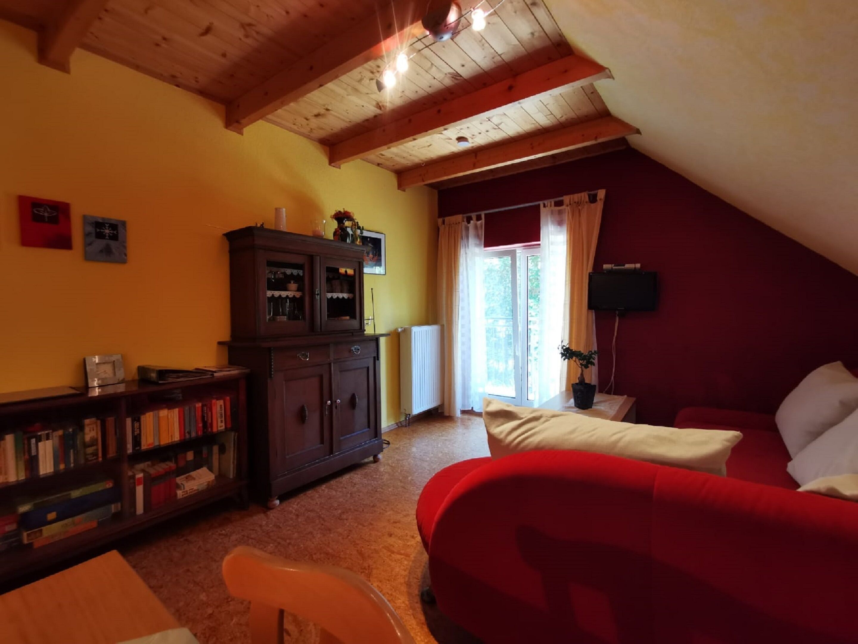 Een knus ingerichte kamer met een rode bank, een houten kast en een boekenplank.