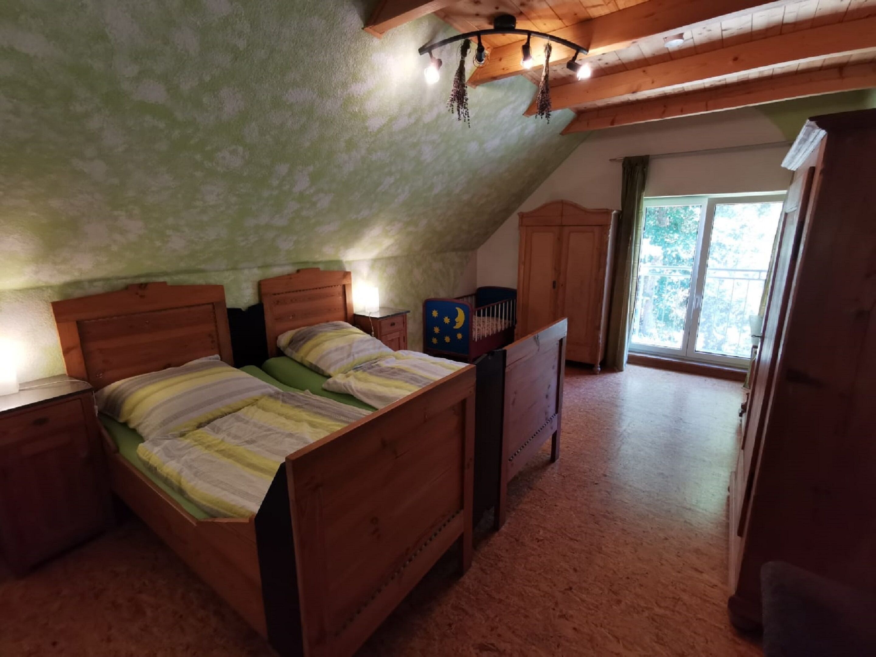 Un dormitorio con techo inclinado, cama de madera, mesitas de noche y ventana con vista a follaje.