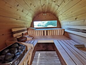 Una sauna con bancos de madera, un banco con respaldo, una mesa de madera y un ventanal con vistas a árboles.