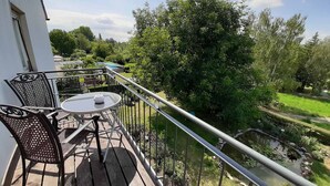 A balcony with a table and chairs, overlooking a garden and a pond. - Gästehaus Edelmann (Gelnhausen)