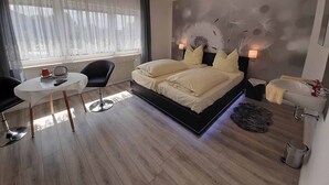 A modern bedroom with a large bed, bedside lamps, a small table, and a chair. - Gästehaus Edelmann (Gelnhausen)
