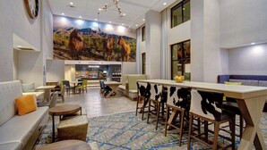 A hotel lobby with a large mural of horses, a bar area, seating arrangements, and a patterned carpet.